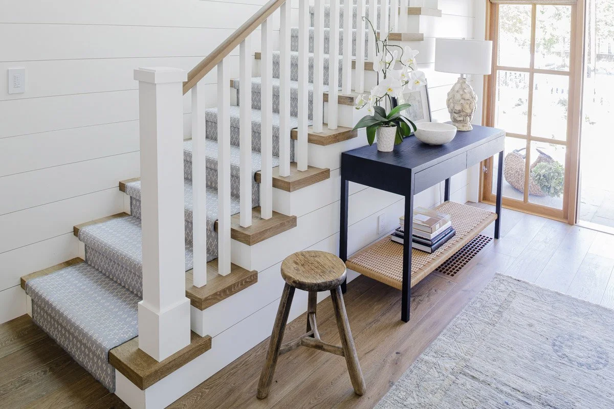 entryway with white staircase, console table and wooden stool