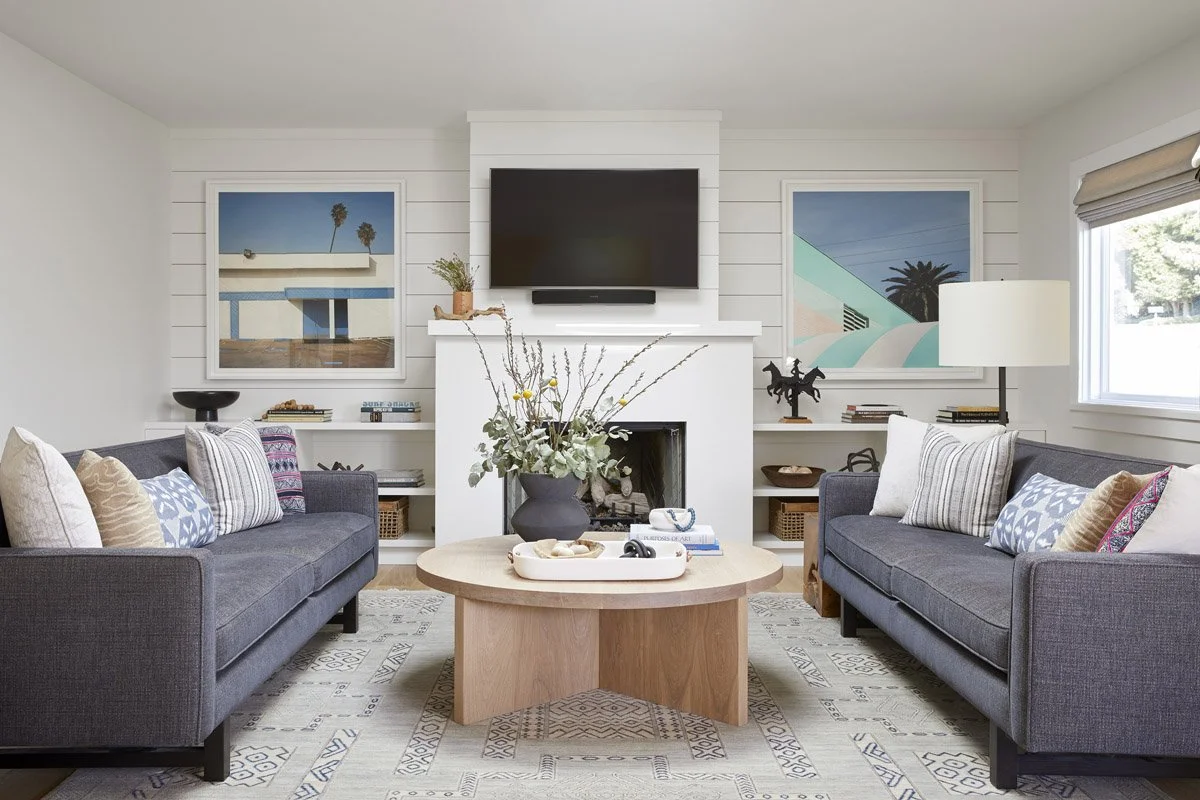 living room with two charcoal sofas facing a round wood coffee table and fireplace