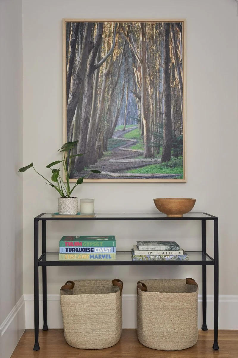hallway console table with woven baskets beneath a large forest painting