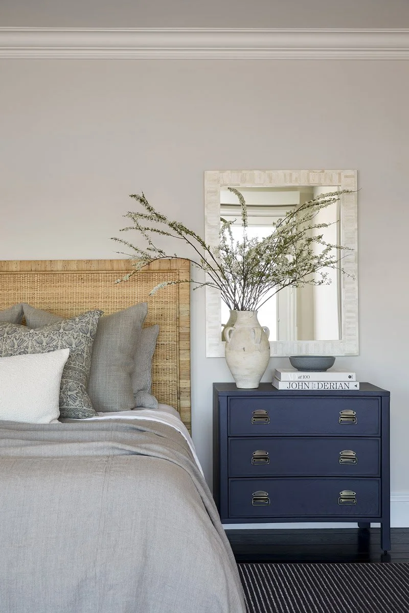 bedside detail with woven headboard, navy dresser and arched mirror