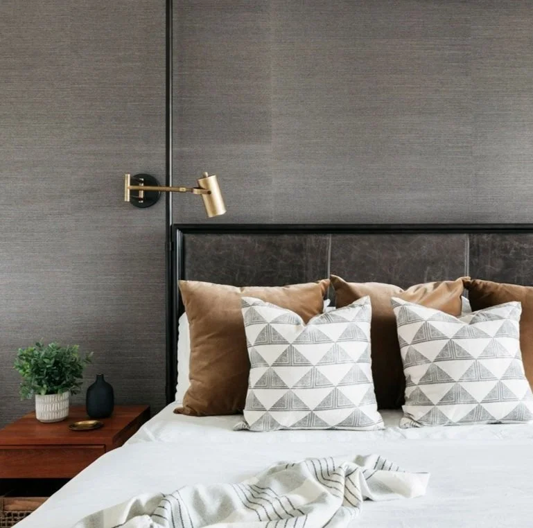 primary bedroom with leather headboard, brass swing-arm sconce and patterned pillows
