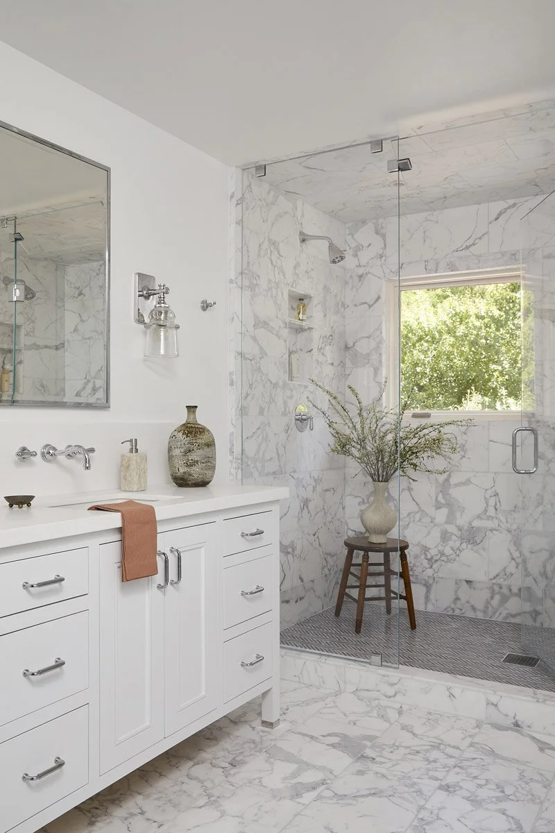 white vanity with marble flooring and a wooden stool by the shower