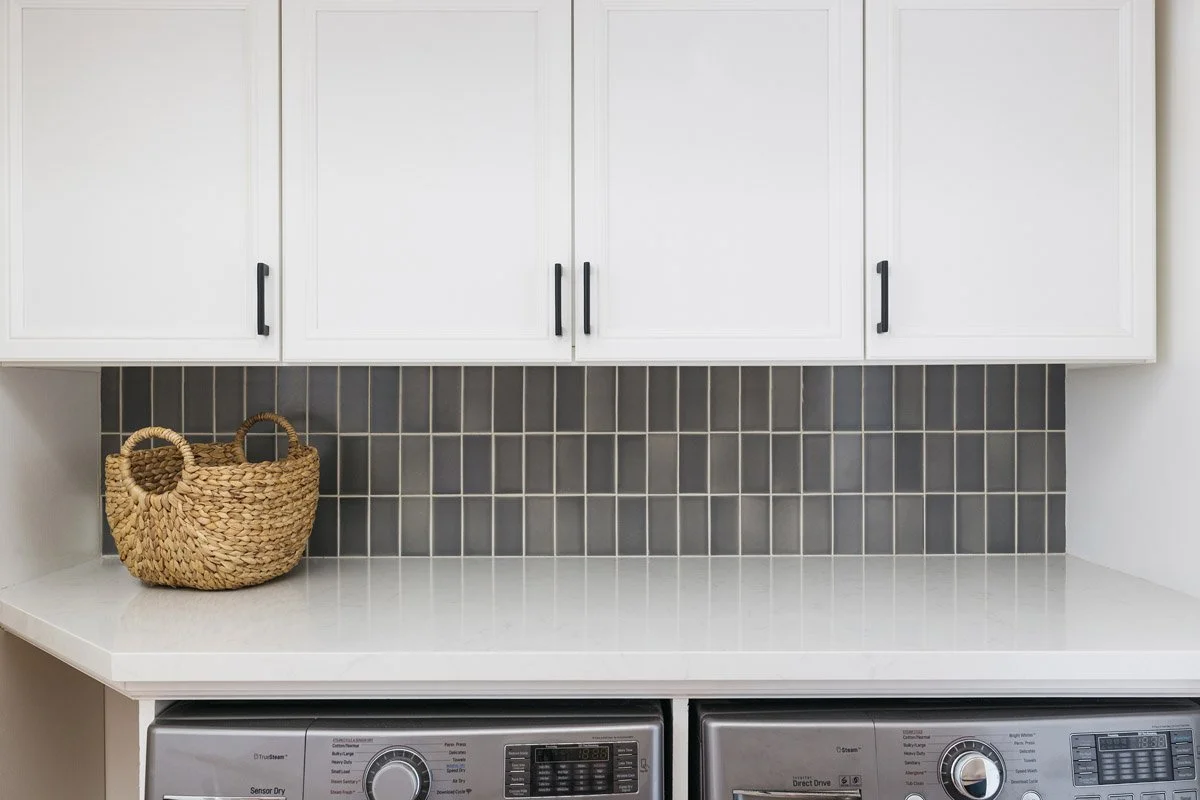 laundry room with grey tile backsplash, white cabinets and woven basket
