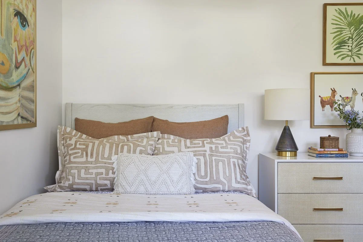 guest bedroom with patterned bedding, white nightstand and framed botanical prints