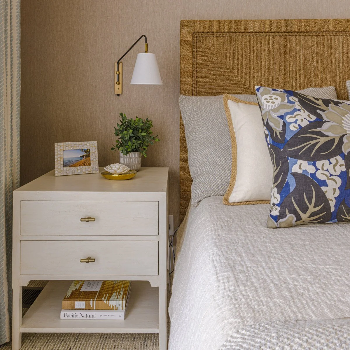 bedside detail with woven headboard, white nightstand and blue floral pillow