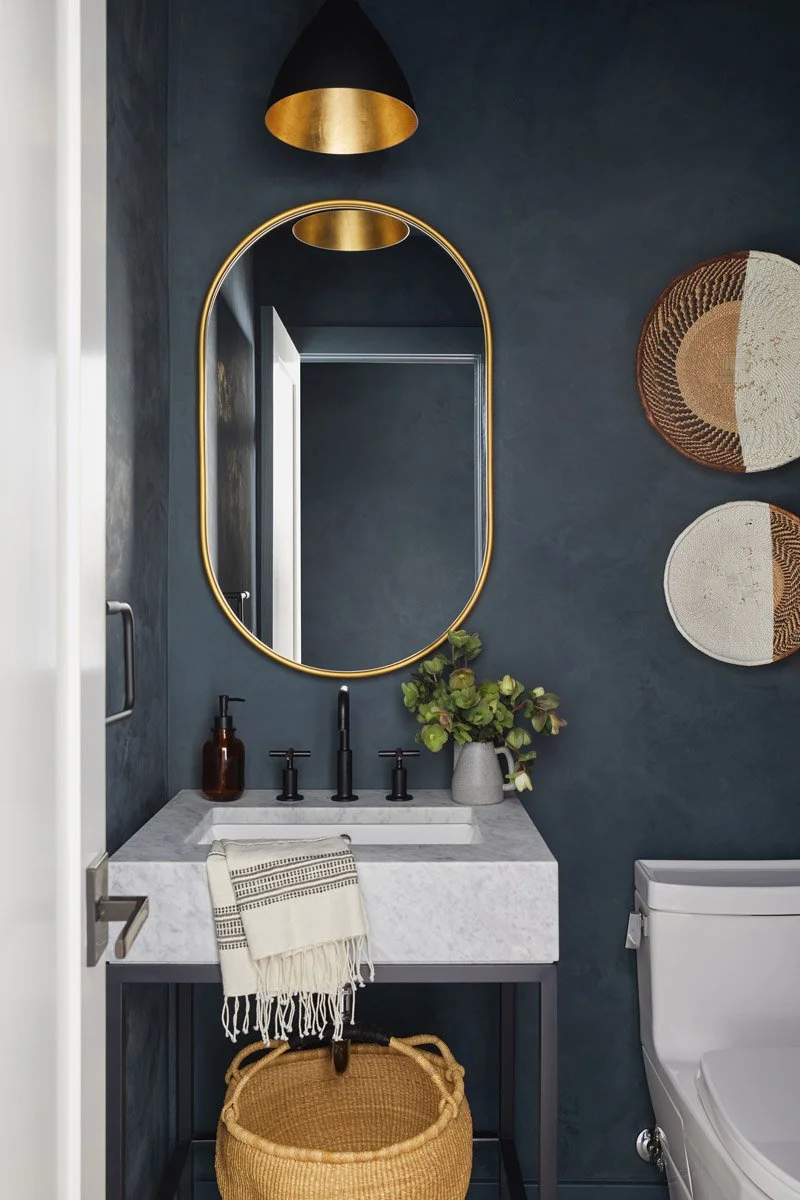 powder room with dark plaster walls, oval brass mirror and stone sink