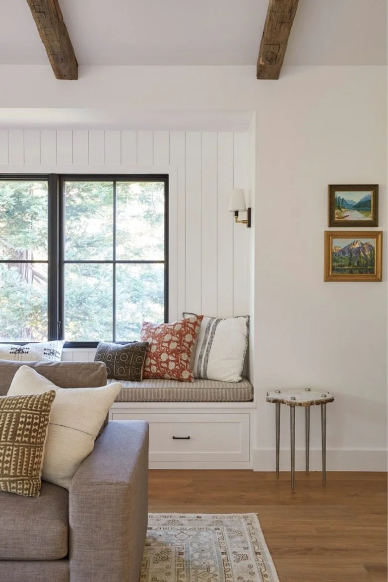 window seat with cushions beside a grey sofa under wood ceiling beams