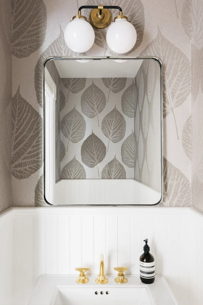 powder room mirror with globe sconce and leaf print wallpaper