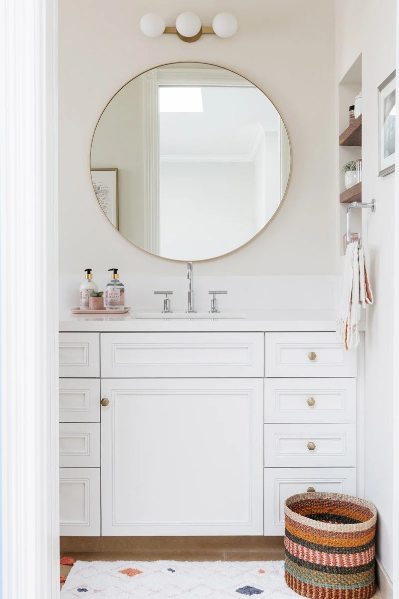 bathroom with round brass mirror, white vanity and patterned bath mat