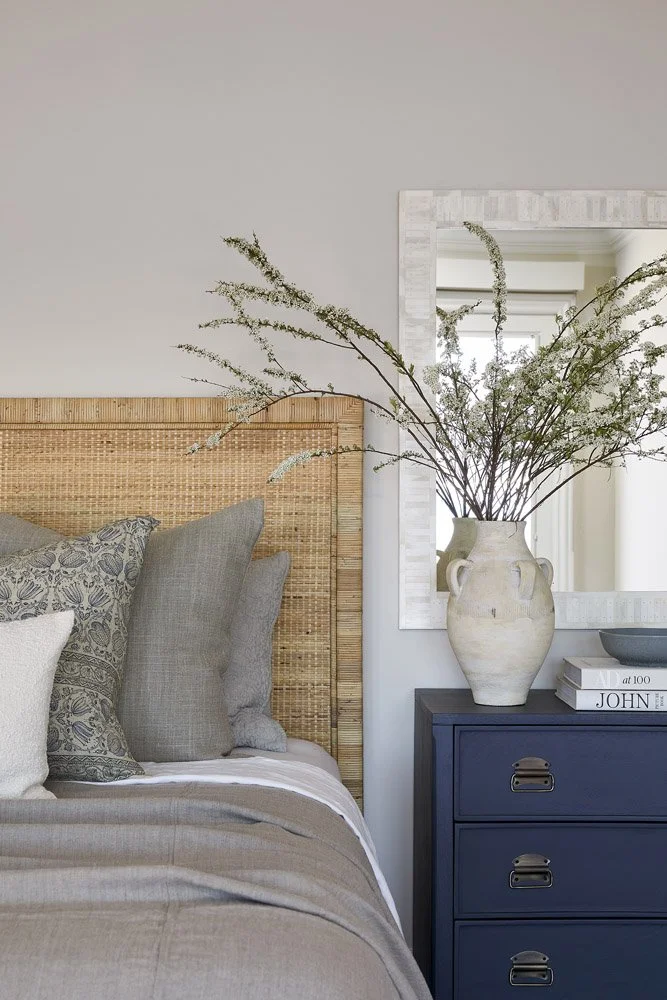 bedroom with woven headboard, navy nightstand and a vase of branches