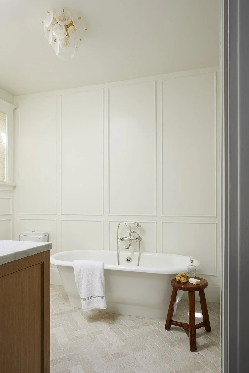 primary bathroom with panelled walls, freestanding tub and wooden stool