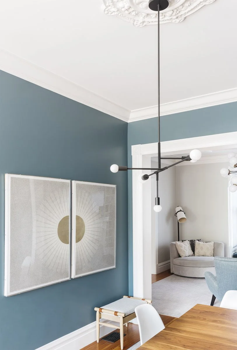 teal dining room wall with framed abstract art and modern pendant