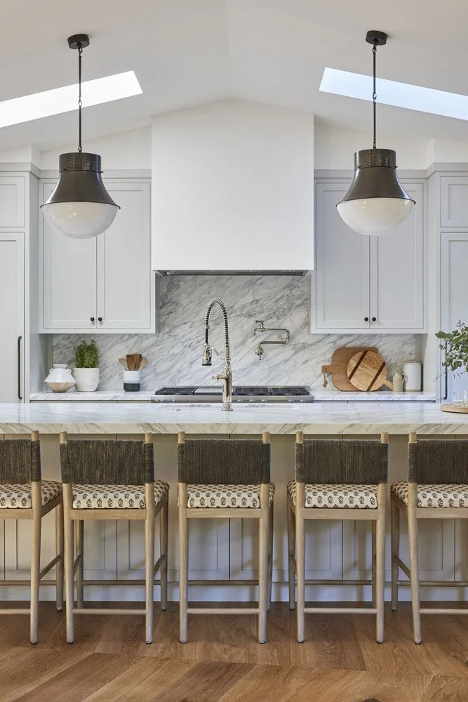 white kitchen with marble backsplash, woven counter stools and black pendant lightswhite kitchen with marble backsplash, woven counter stools and black pendant lights