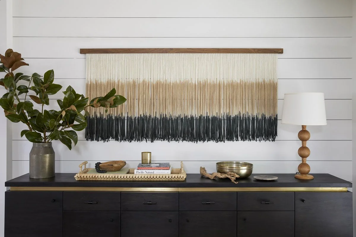 black sideboard with dip-dyed fibre wall hanging and wooden table lamp