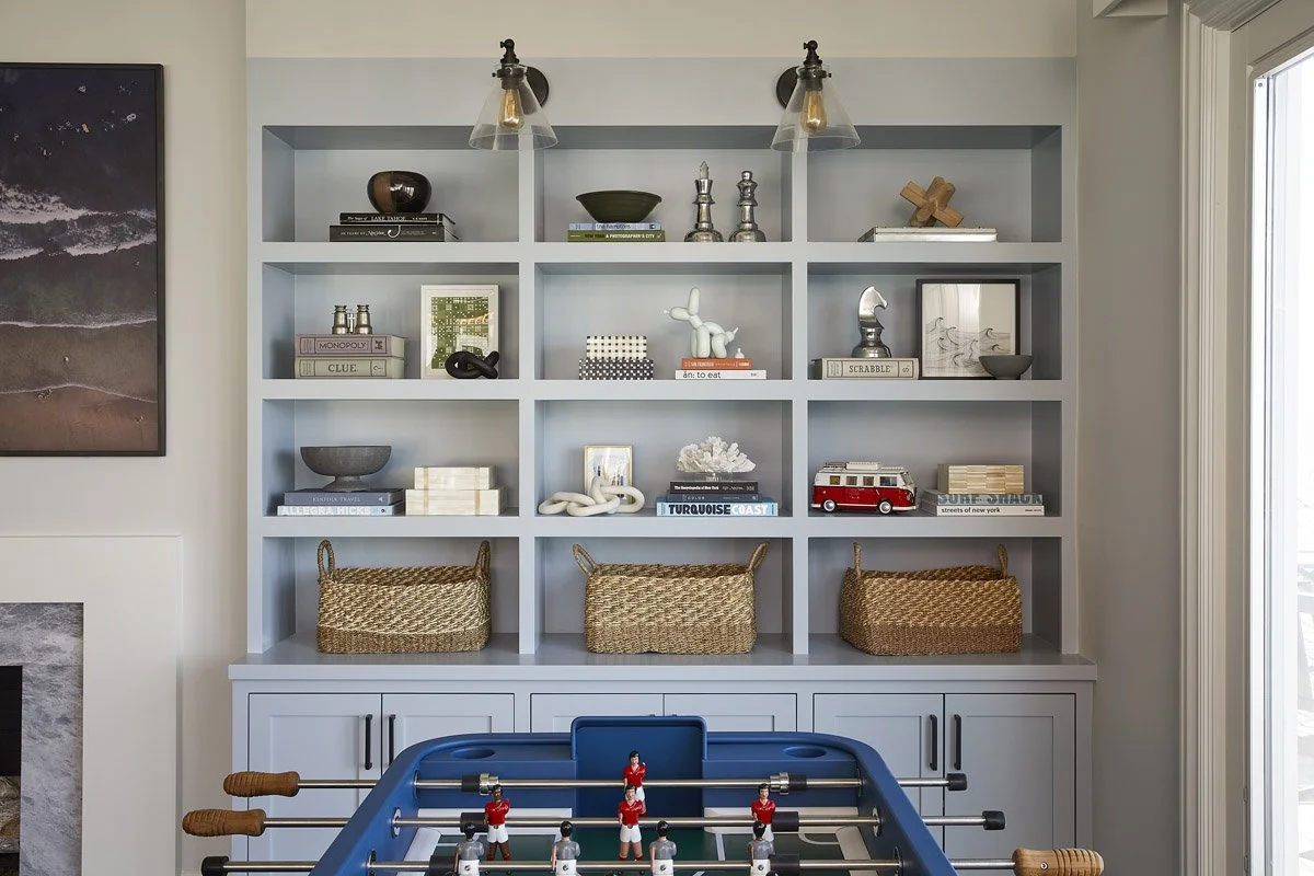 pale blue built-in bookcase with woven baskets above a foosball table