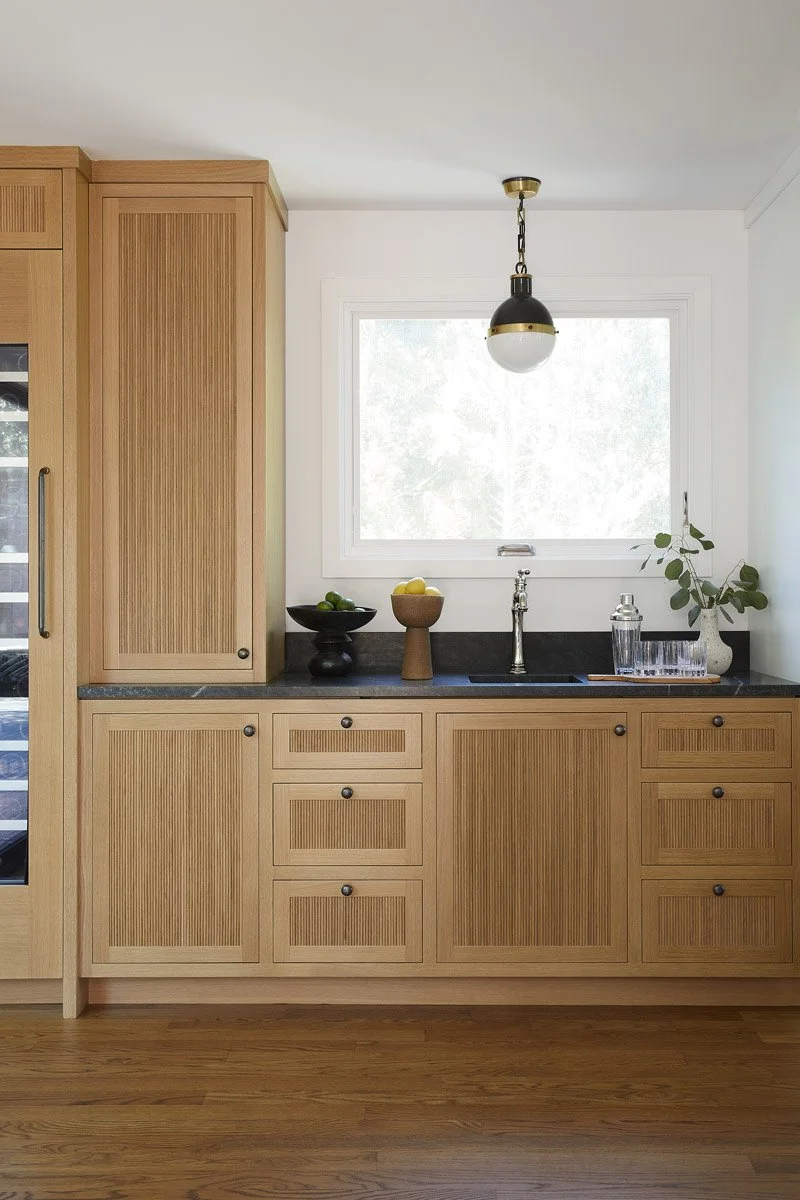 white oak kitchen cabinetry with black countertop and glass pendant light