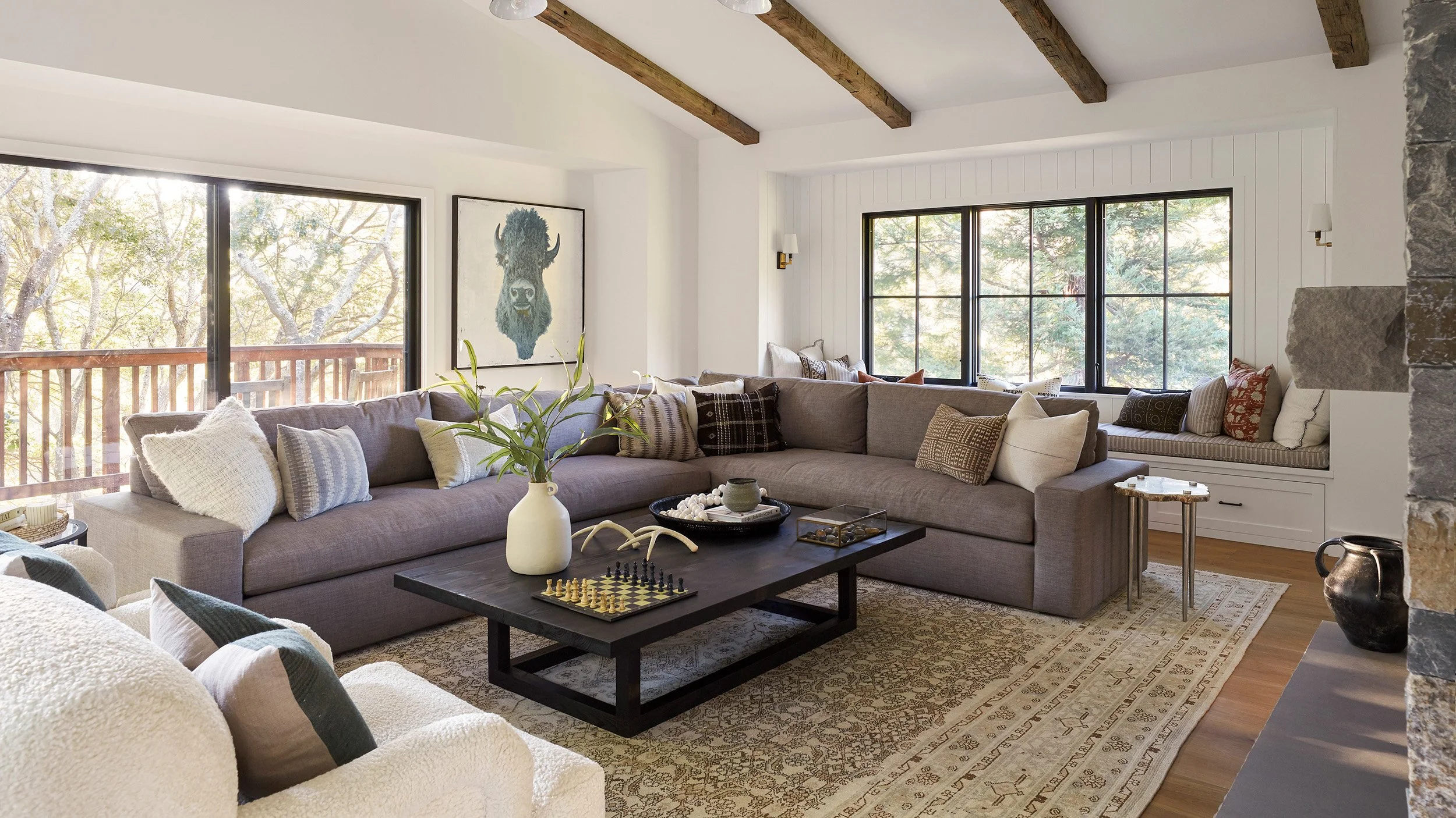great room with grey sectional sofa, wood beam ceiling and large black windows