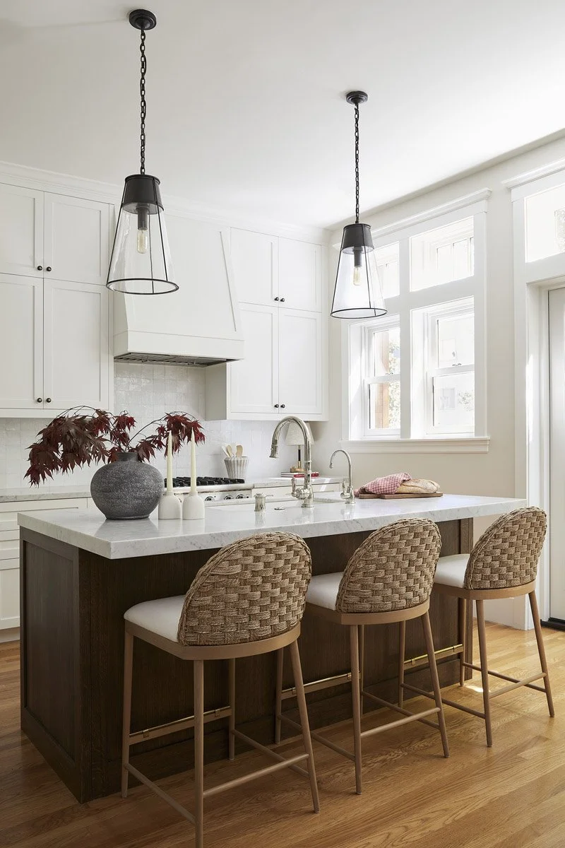 kitchen island with woven stools, glass pendant lights and white cabinetry