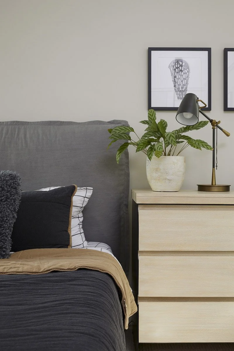 bedside detail with charcoal headboard, light wood dresser and potted plant