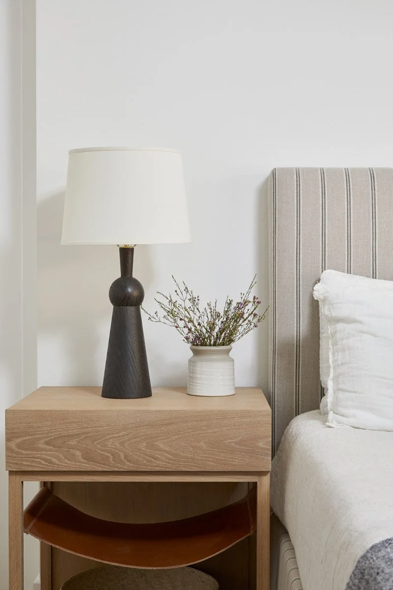 bedside table with black ceramic lamp beside a channelled upholstered headboard