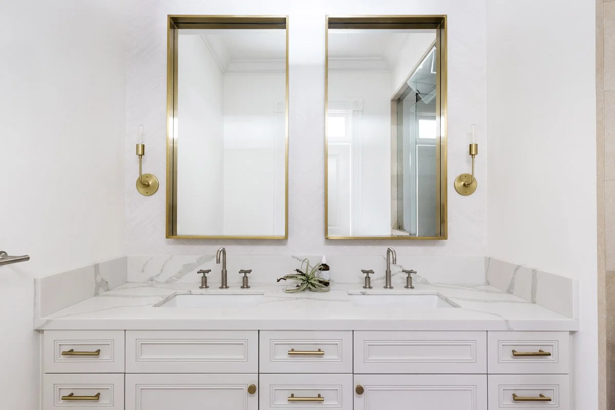 primary bathroom with white double vanity, brass mirrors and sconces