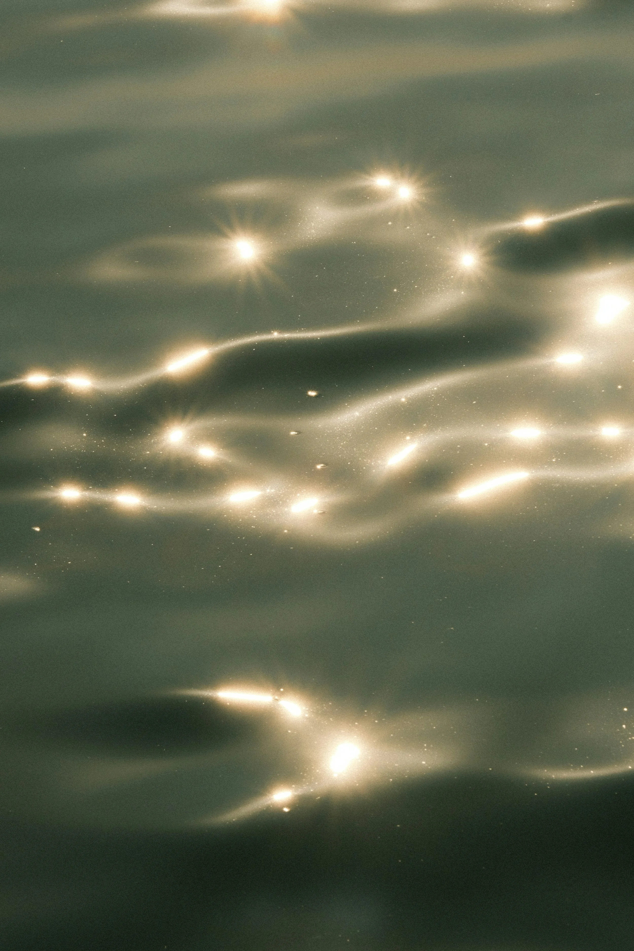 Close-up of a surface with reflective, glowing streaks and bright spots resembling light reflections or star-like points, with a dark, muted background.
