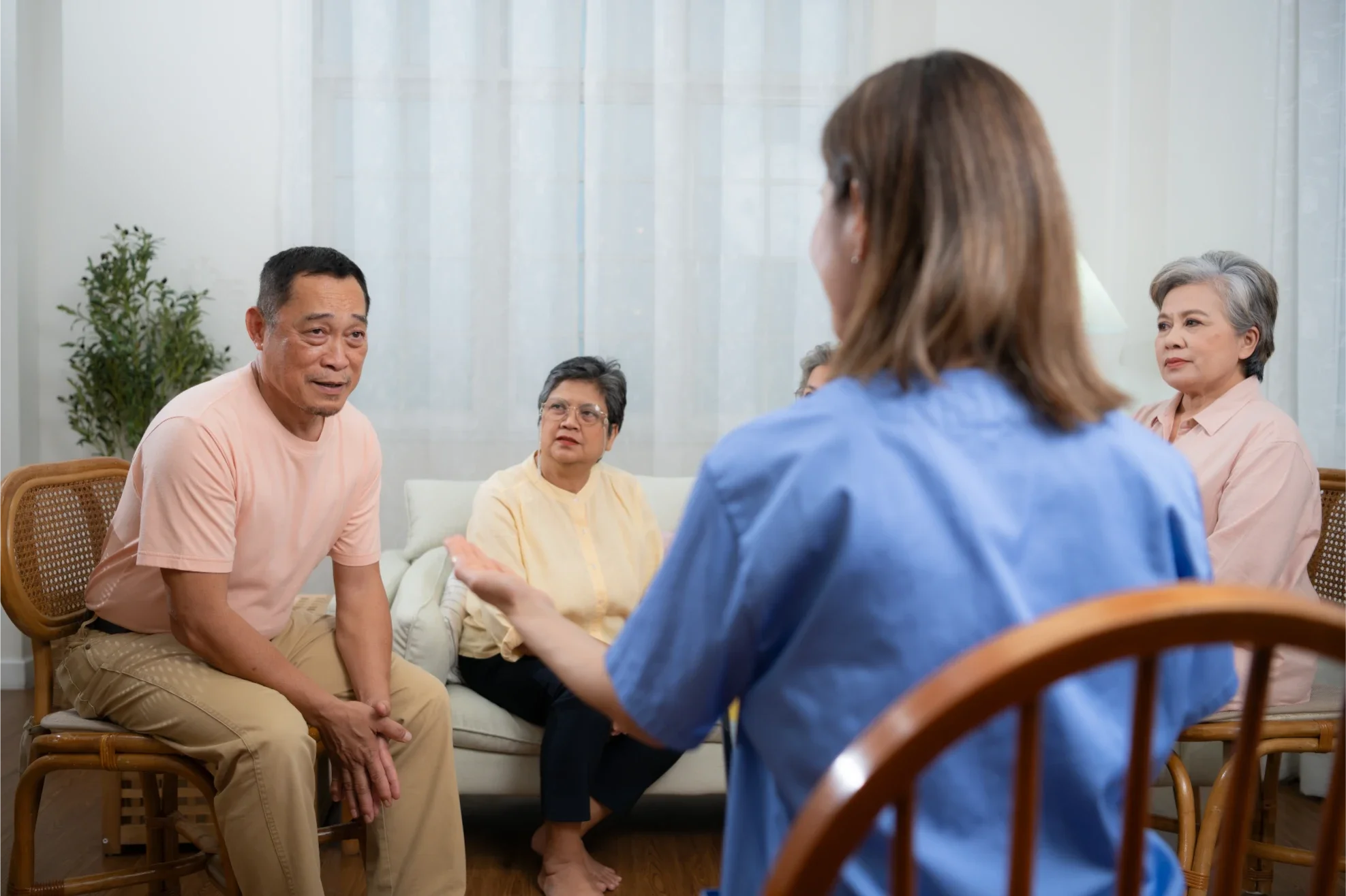A group of elderly adults and a caregiver having a conversation in a living room.