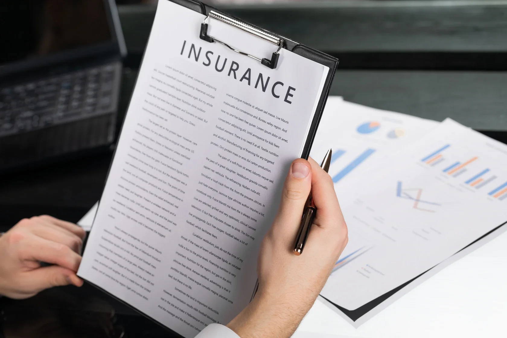 A person holding a clipboard with an insurance document, and there are printed charts and graphs on paper on the table.