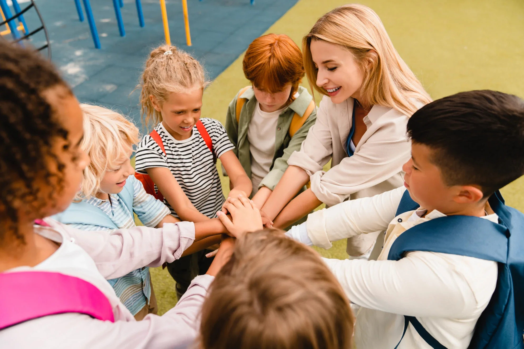 Children and teacher joining hands in a circle at school playground.