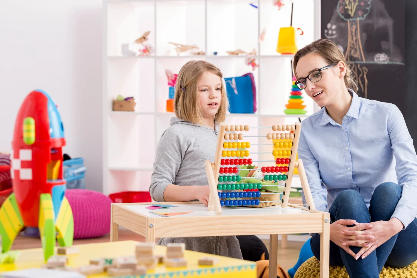 A young girl and a woman playing with an abacus in a brightly decorated room.