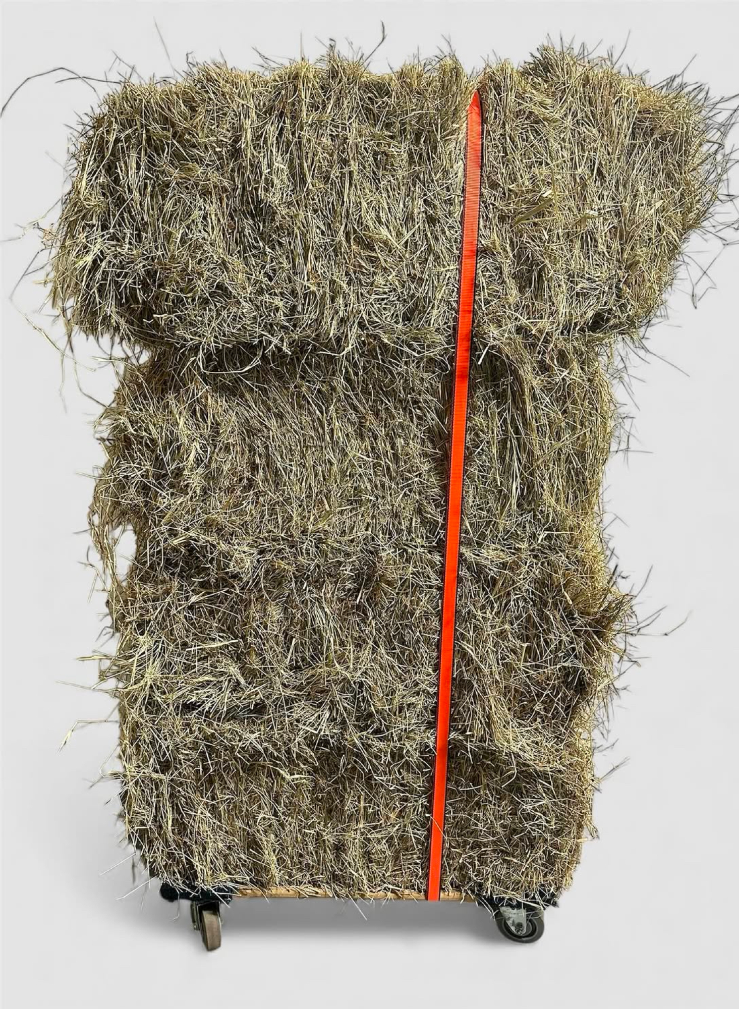 sculpture of piles of hay held together by a bright orange strap on a dolly