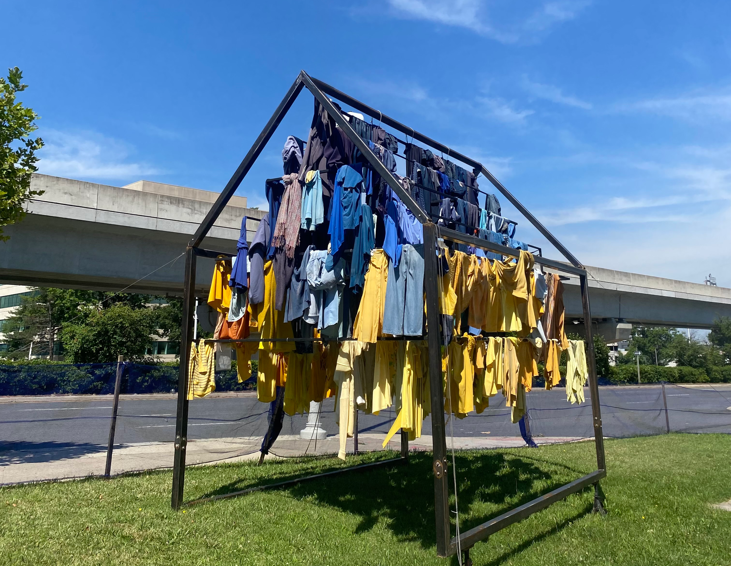photograph of steel house frame on grass with clothes hanging off it in shades of yellows and blues