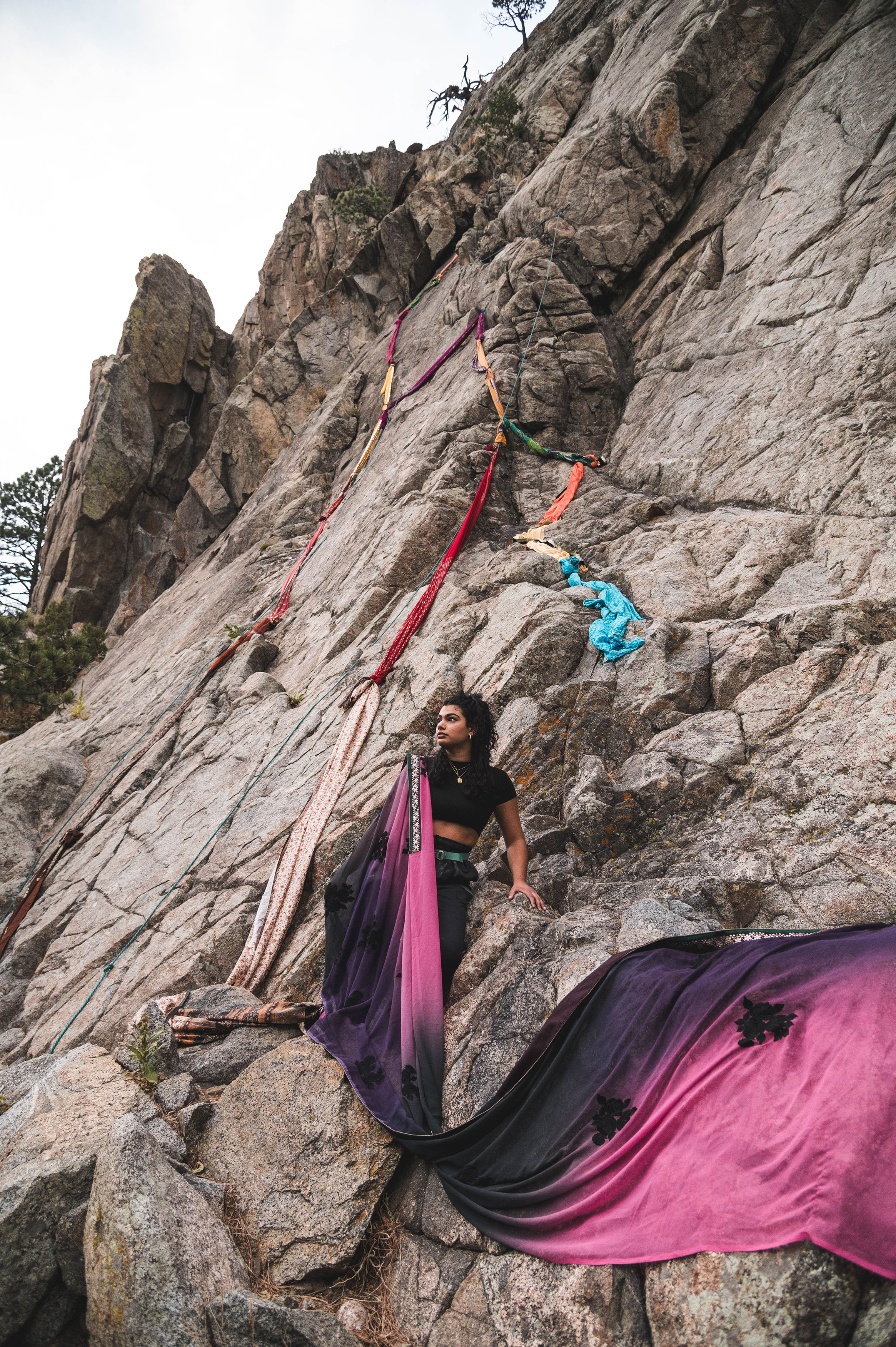 Brown skin women standing holding long rope fabric flowing down rock surface