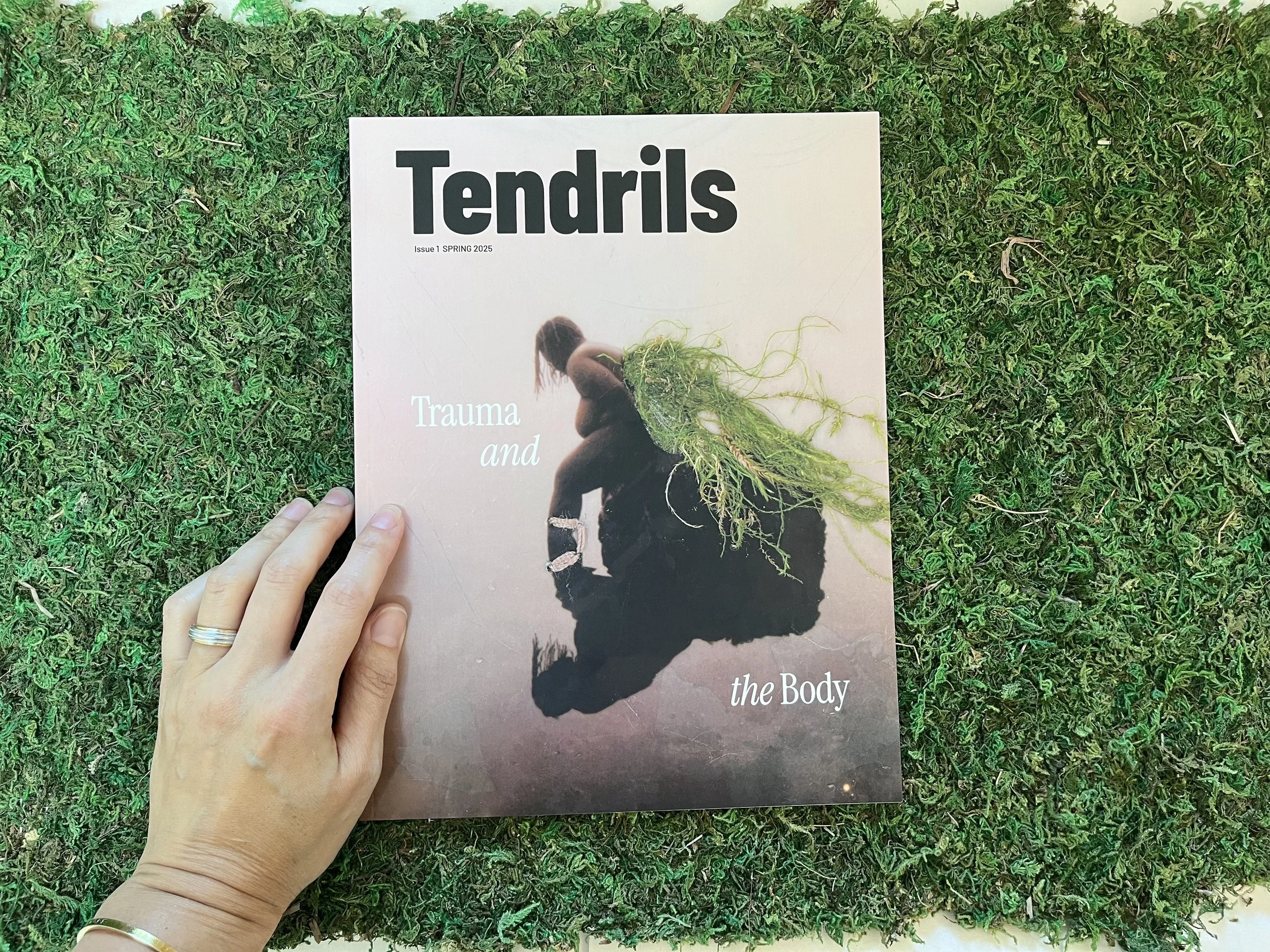 left hand touching Tendrils journal cover on grass background