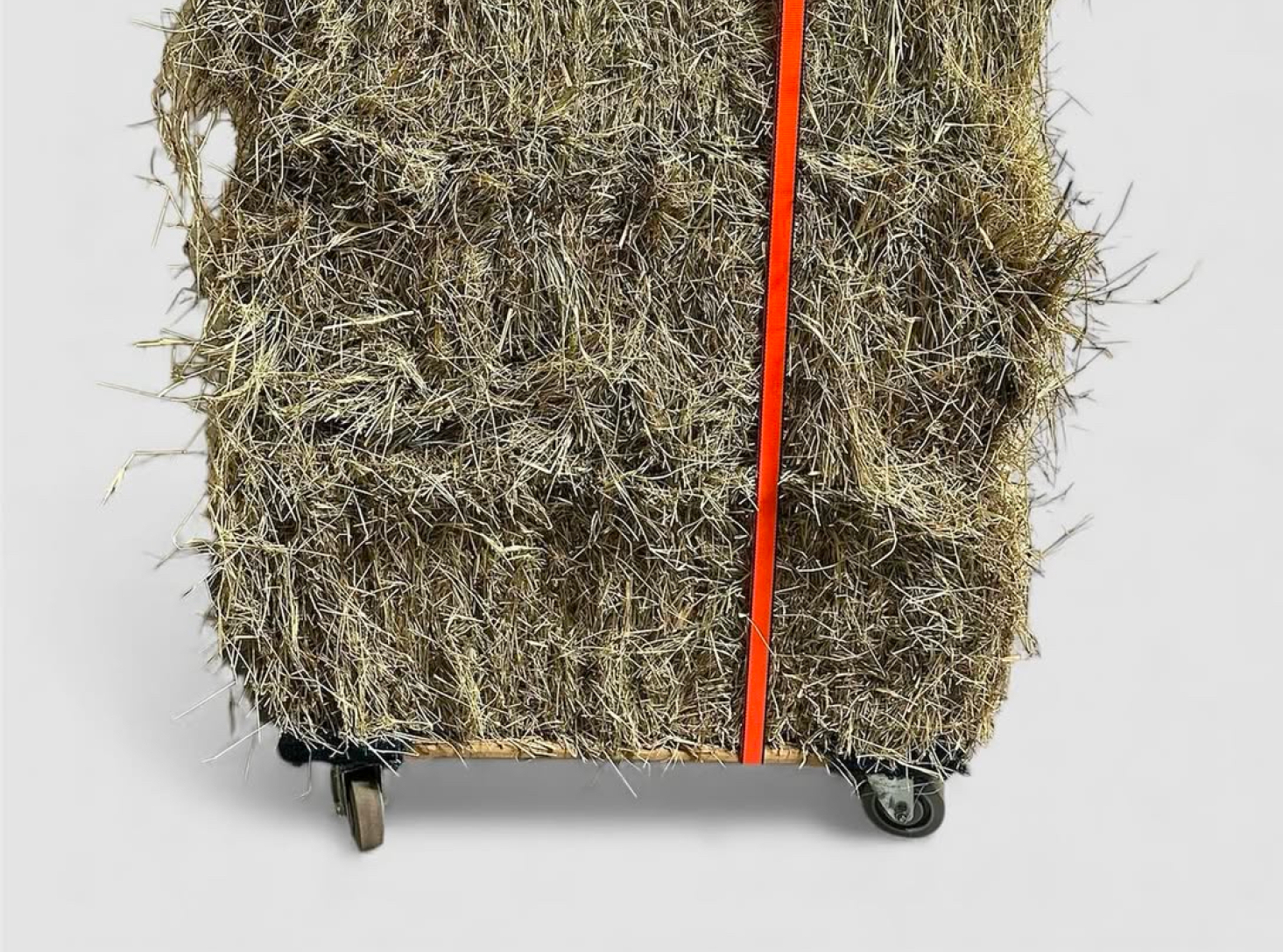 sculpture of piles of hay held together by a bright orange strap on a dolly