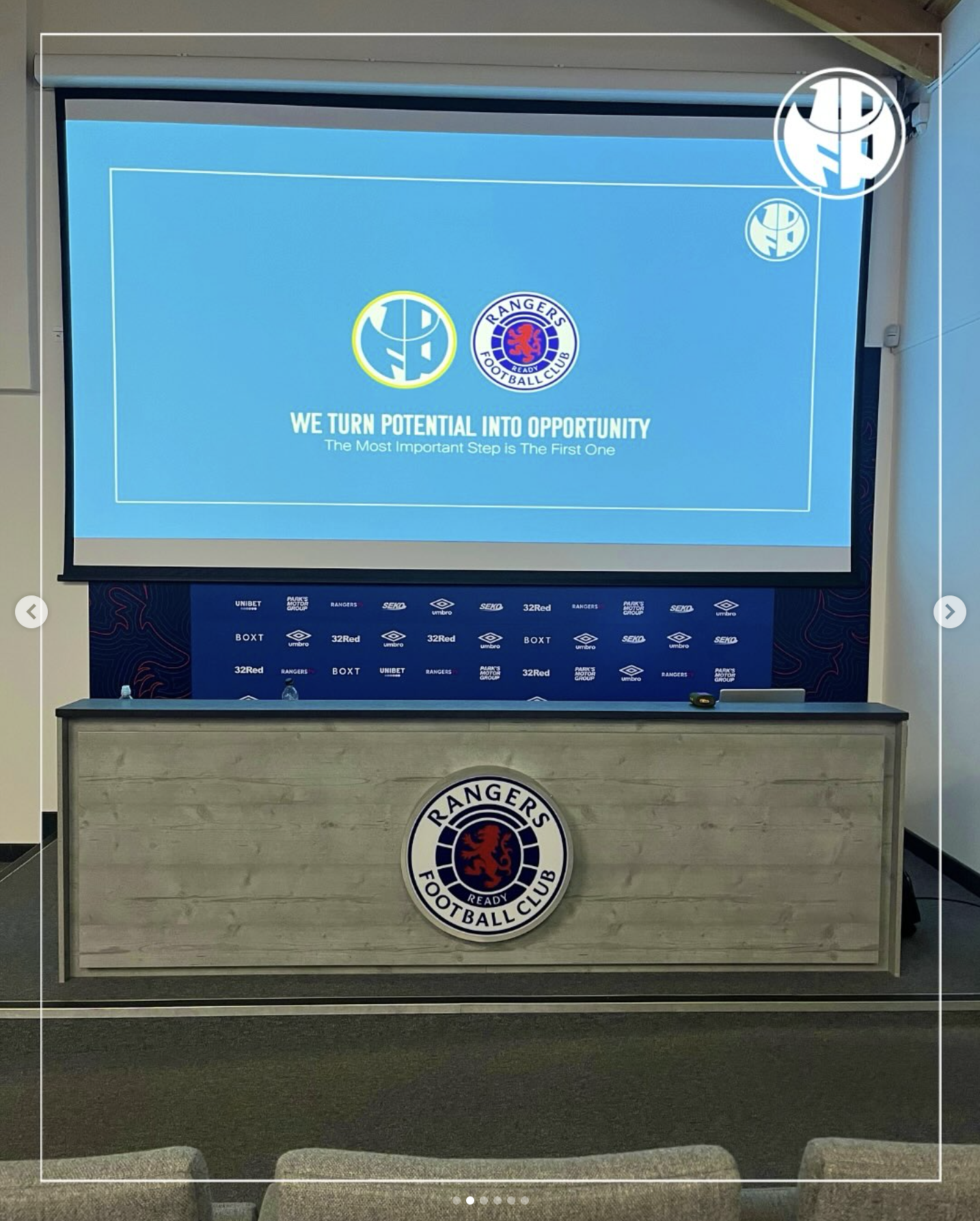 A conference room with a large screen displaying the Rangers Football Club logo, alongside the slogan "We turn potential into opportunity," and a table with the Rangers logo on the front.