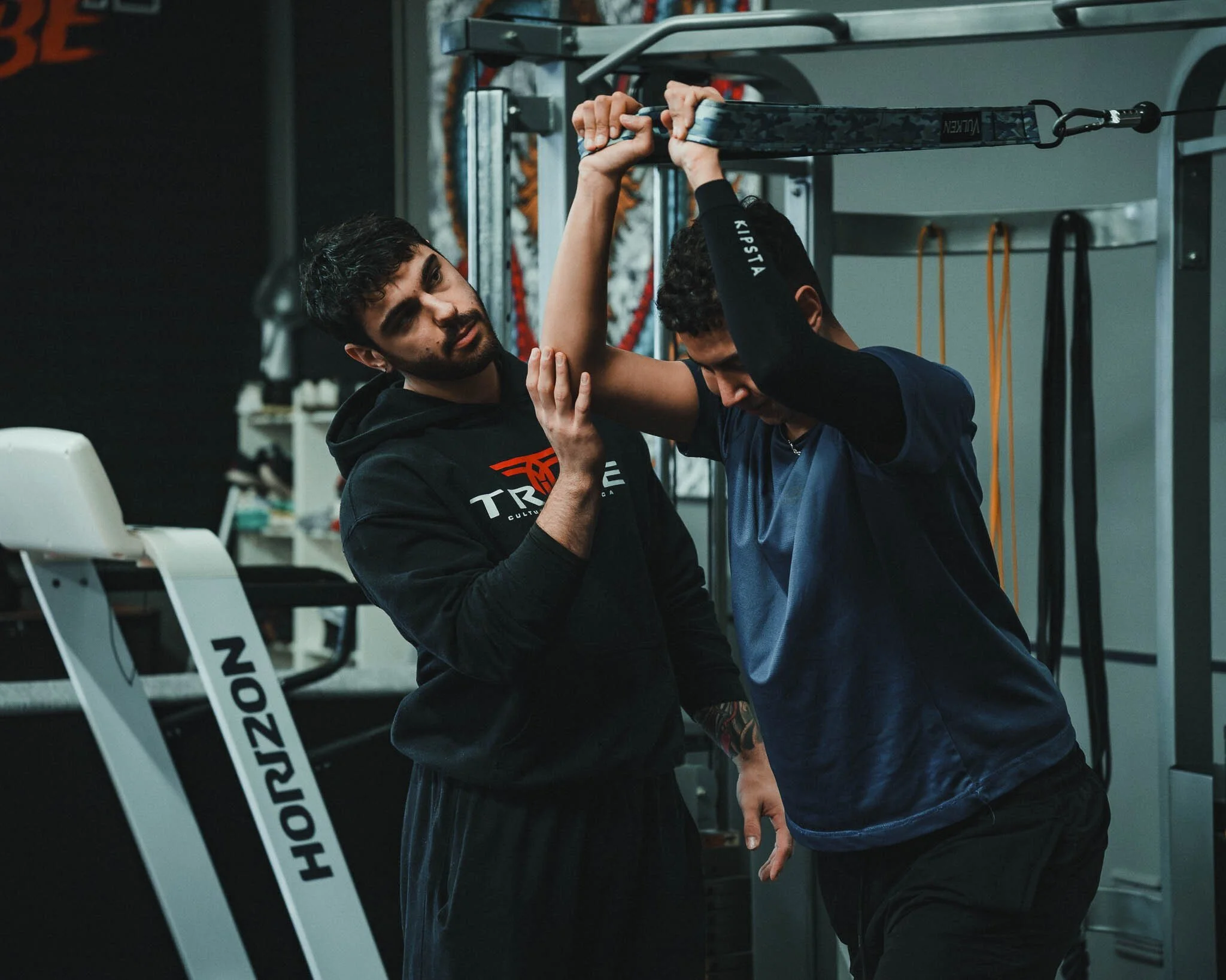 Due persone si allenano in una palestra, una che aiuta l'altra con gli esercizi alla barra di trazione.
