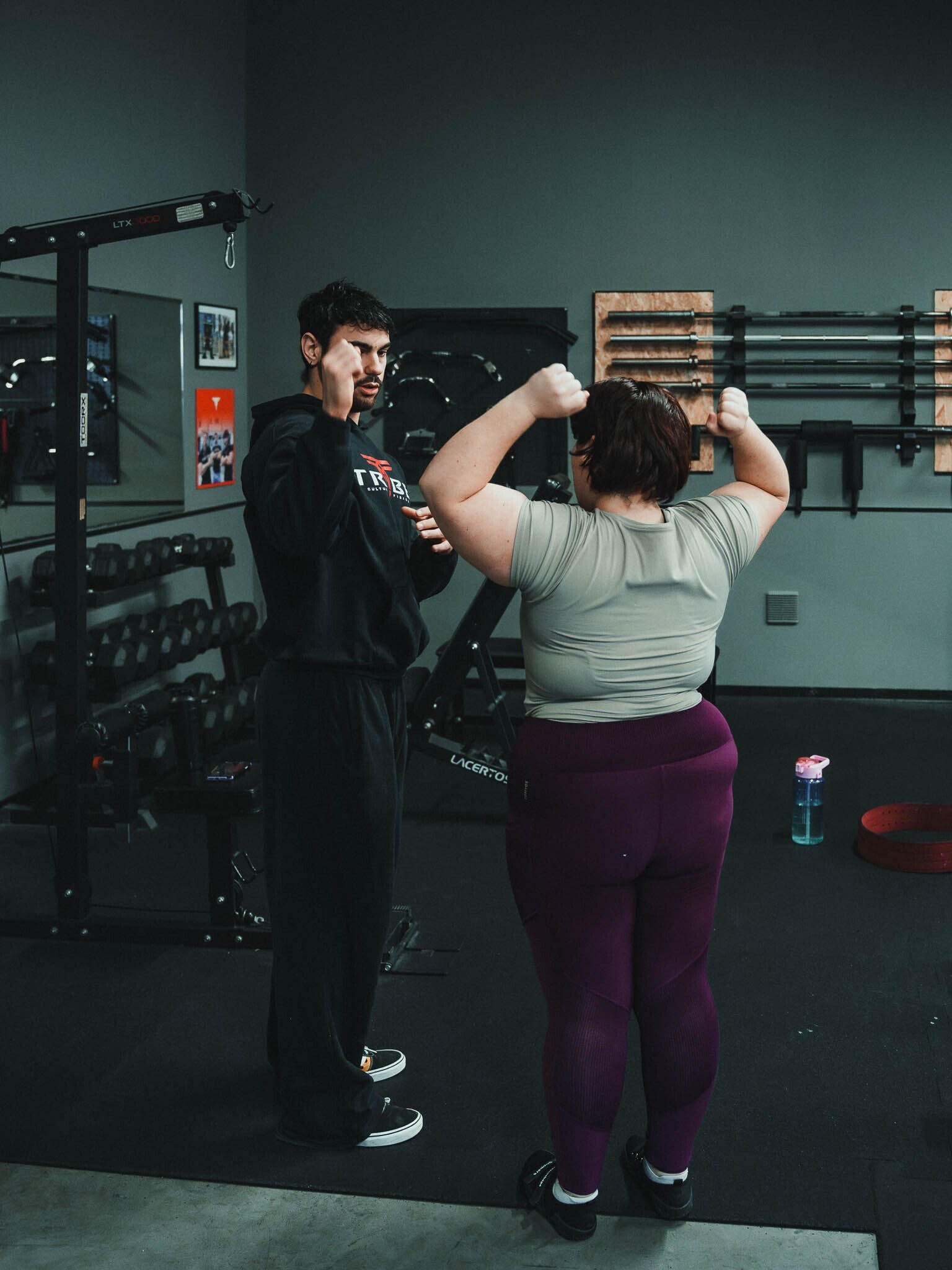 Una donna sta facendo esercizi di bicipiti con il personal trainer in una palestra, entrambi sollevano le braccia con i pugni chiusi.