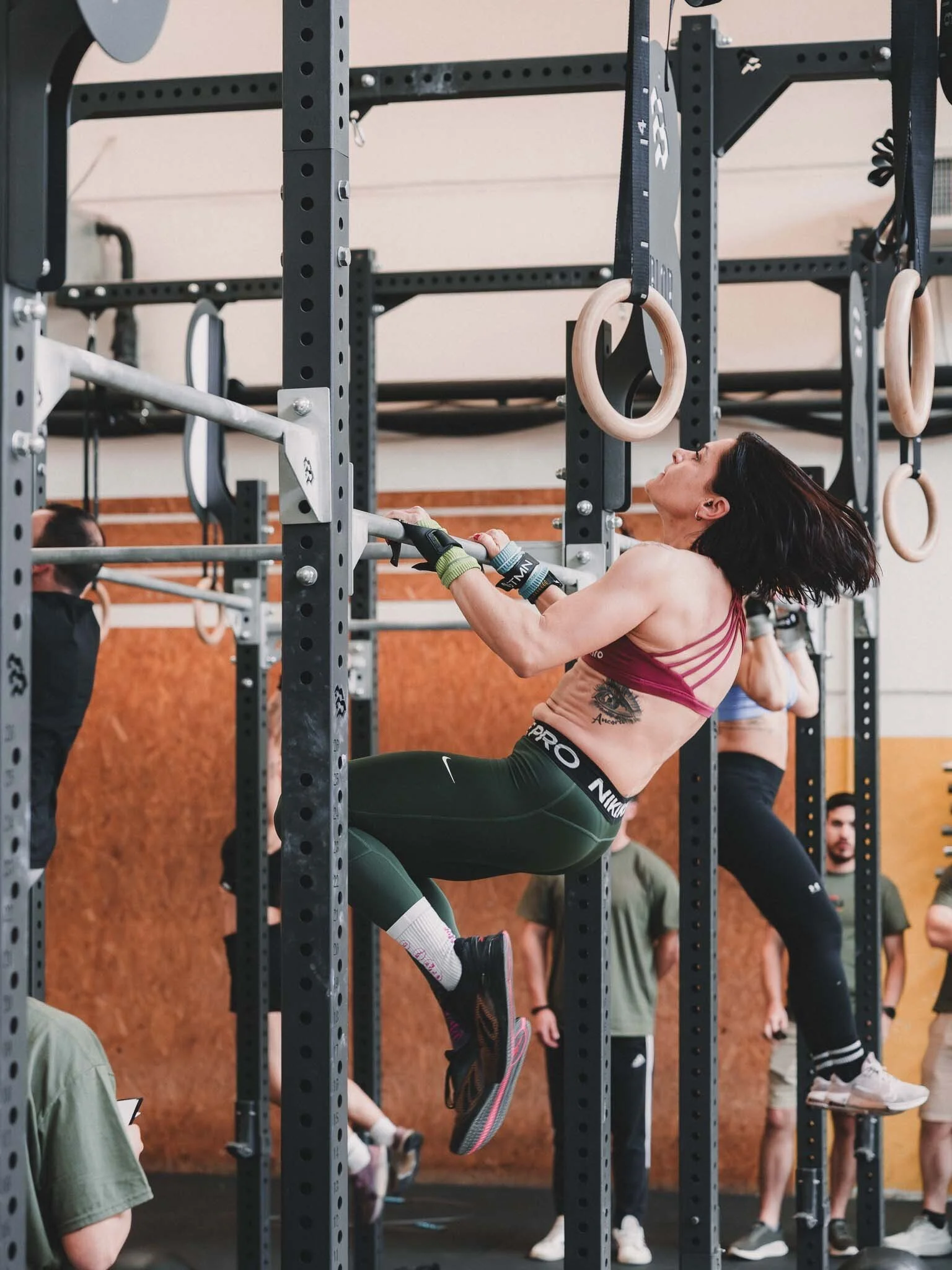 Una donna sta facendo esercizi di trazione alle s rings in una palestra, circondata da altre persone che si allenano.