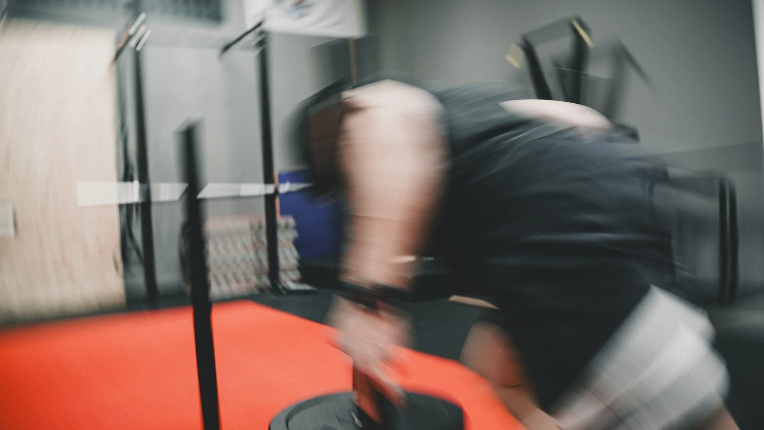 Una persona si allena in palestra, abbassata con il volto vicino al pavimento, con attrezzature e pareti di colore grigio sullo sfondo.