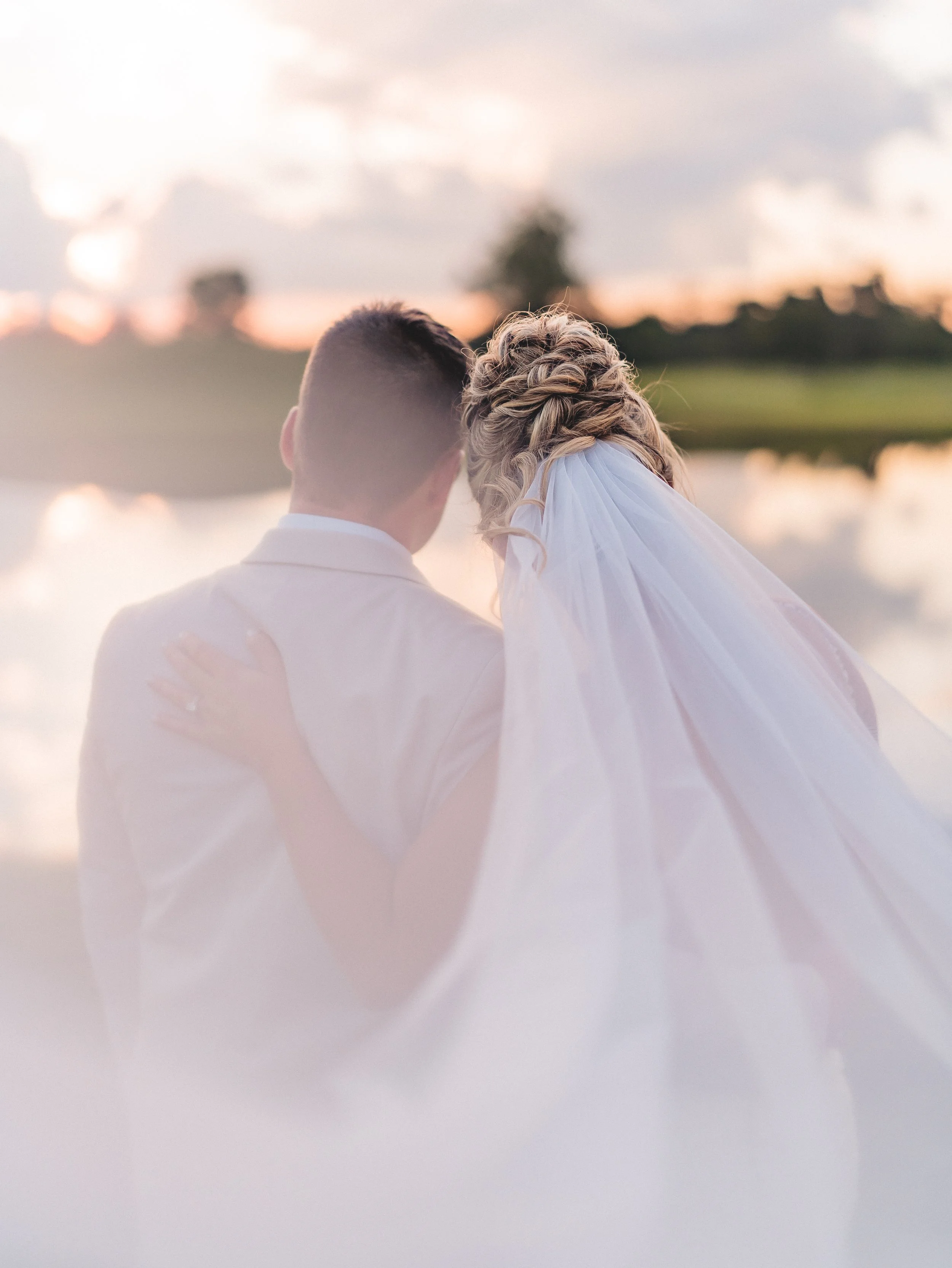 newlyweds sit facing a lake during sunset
