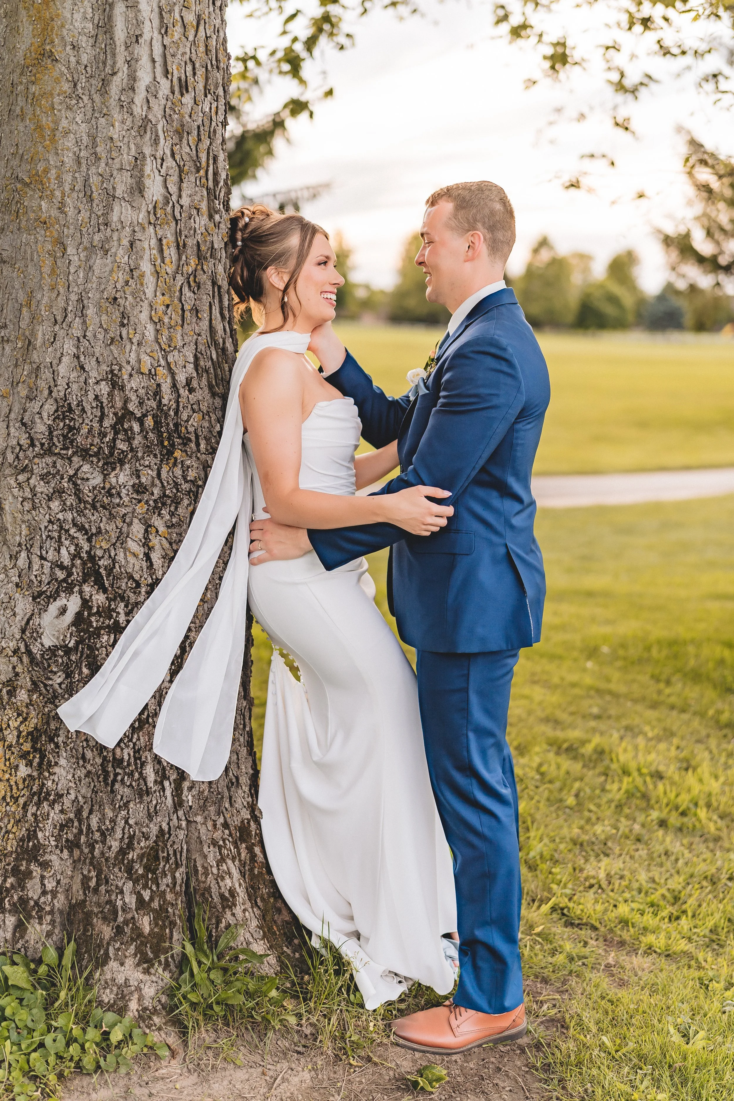 bride and groom lean against a tree sunset