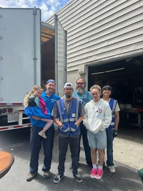 Group of five people standing in front of a moving truck and a garage, with one woman holding a young girl.