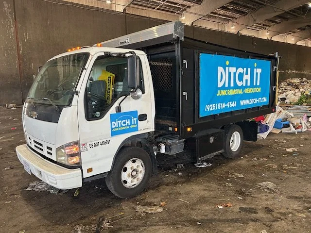 A junk removal truck labeled DITCH IT parked inside a warehouse with trash and debris on the ground.