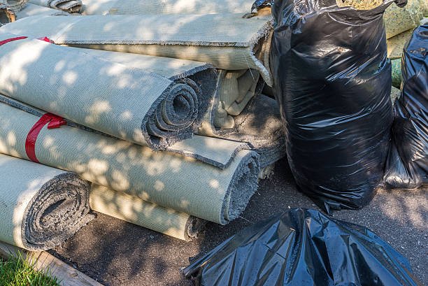 Rolled-up carpets and black trash bags on pavement in outdoor setting.