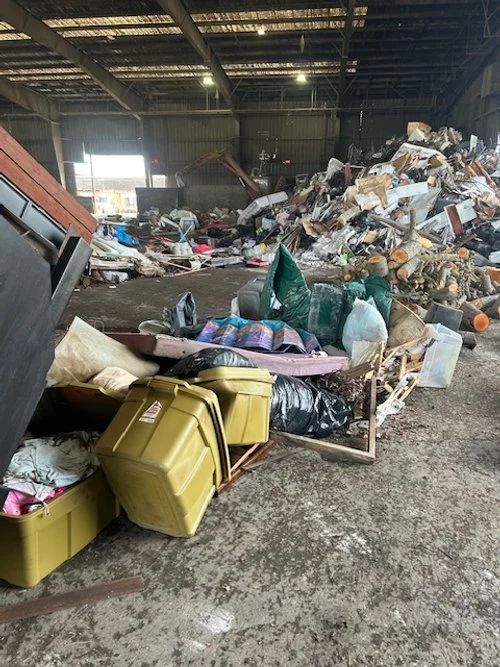 Indoor area filled with large piles of various trash and debris, including plastic bins, bags, and discarded items.