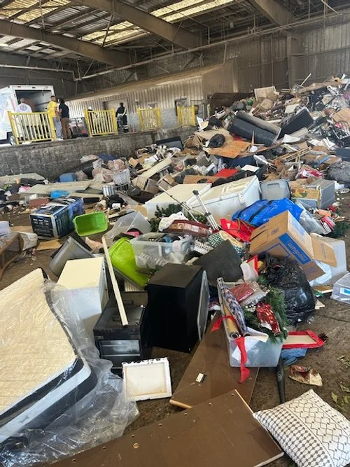Overfull indoor space with trash and discarded items scattered around, including furniture, boxes, electronics, and household items.