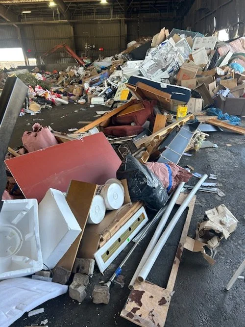 A large pile of discarded furniture, boxes, and miscellaneous debris in a warehouse or industrial space.