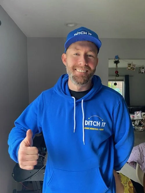 Man wearing a blue hoodie and cap with the text 'DITCH IT' giving a thumbs-up inside a home, smiling at the camera.