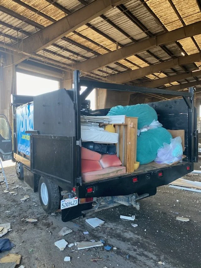 A moving truck packed with furniture and large bags, parked inside a warehouse or garage with a high ceiling.